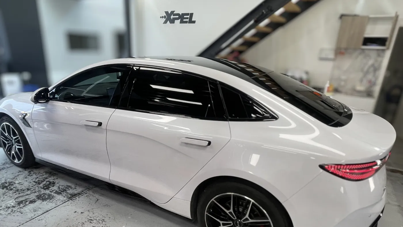 White sedan with tinted windows in a workshop with an XPEL sign on the wall
