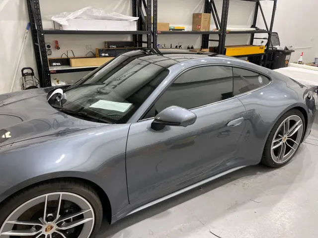 Grey Porsche 911 with tinted windows beside shelves of XPEL film boxes